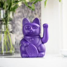 Charger l'image dans la galerie, Figurine Maneki Neko violette sur une étagère blanche, avec un vase de fleurs en arrière-plan, vue de face.